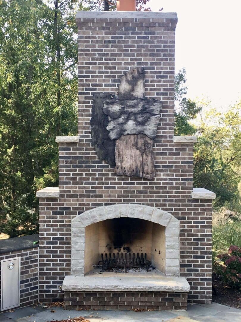 Outdoor brick fireplace with decorative stone relief in a garden setting.