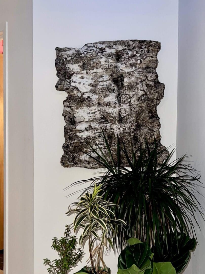 Textured abstract wall art above leafy houseplants in a minimalist setting.