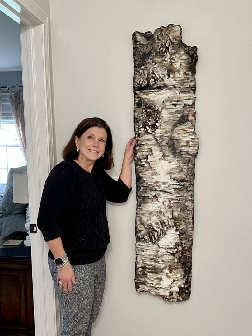 Woman standing next to a tall, textured birch bark art piece.