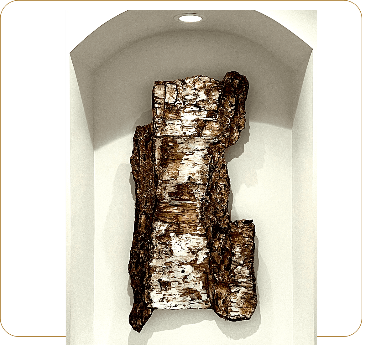 A rectangular bark-like sculpture displayed in a white niche.
