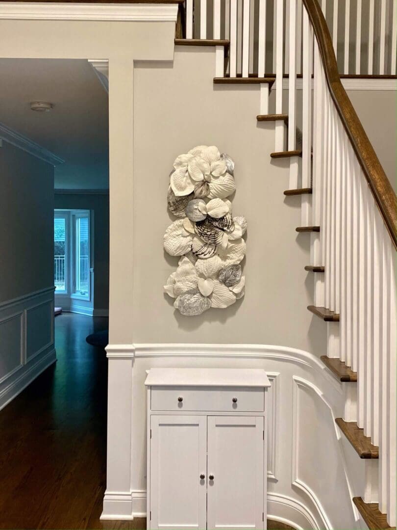 White floral wall sculpture beside staircase and cabinet.