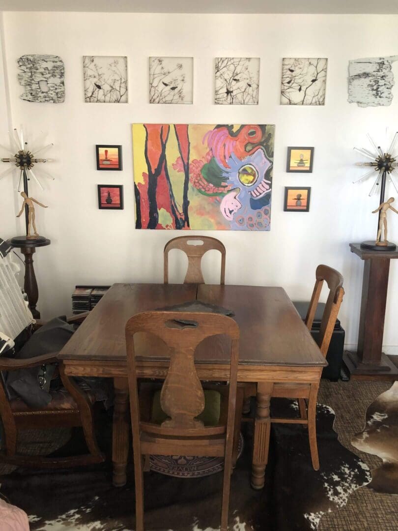 Vintage wooden dining table with chairs in a cozy room adorned with colorful wall art.