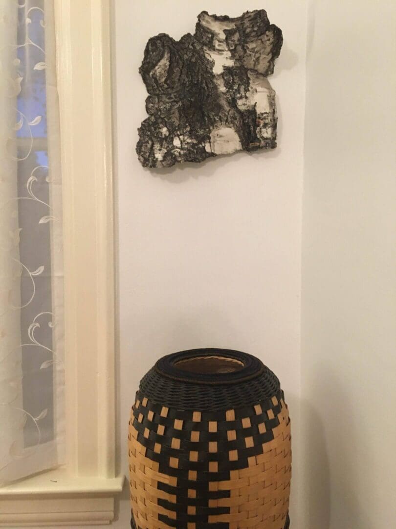 Decorative vase with geometric patterns on a wooden stand beside a sheer curtain.