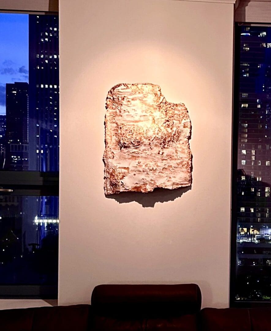 Abstract art piece illuminated on a white wall with city lights outside.