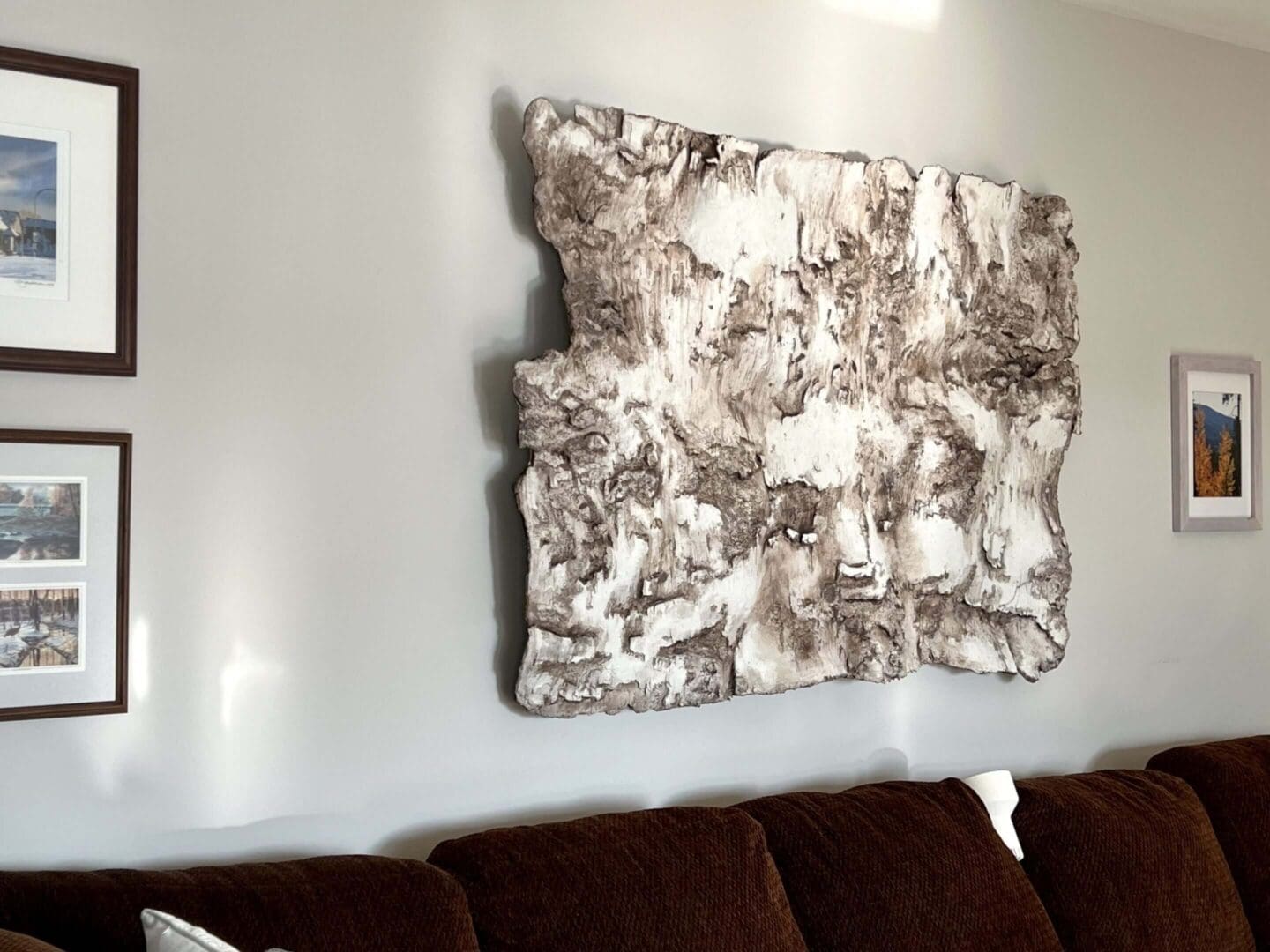 Abstract textured wall art hanging above a brown couch.